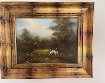 Könnte beinhalten: Ein Ölgemälde in einem breiten, antik wirkenden goldfarbenen Rahmen zeigt eine Landschaft mit einem weiß-braunen Hund auf einer Wiese. Im Hintergrund sind dichte grüne Bäume und ein heller Himmel mit einem fliegenden Vogel zu sehen.