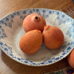 May include: A white ceramic bowl with a scalloped edge and a blue floral pattern containing three round, terracotta-colored objects with small circular openings at the top. Additional similar terracotta objects are placed outside the bowl.