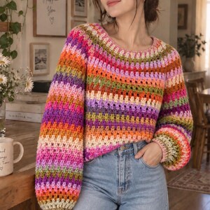 Peut inclure: Un pull en crochet à manches longues présentant un motif rayé multicolore vif dans des tons de rose, orange, violet, vert et crème. Le vêtement possède une encolure ronde, des manches amples et est porté avec un jean en denim bleu clair.