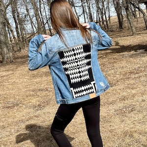 May include: A blue denim jacket with a black and white geometric pattern on the back.