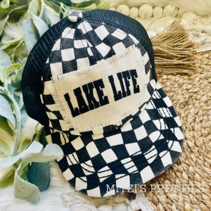 May include: Black and white checkered trucker hat with a mesh back. The front panel features a burlap patch with the words "LAKE LIFE" in bold black letters. A stylish accessory for lake lovers.