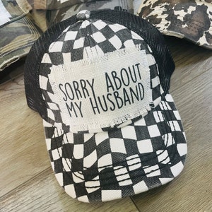 May include: A black and white checkered trucker hat with a white patch that says "Sorry About My Husband".