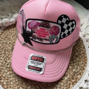May include: Pink trucker hat with a black chain, a patch that says "This Actually Is My First Rode", and a black and white checkered heart patch. The hat has a white label that says "Otto World Famous Foam Front OSFM Trucker Durable Snap Closure".