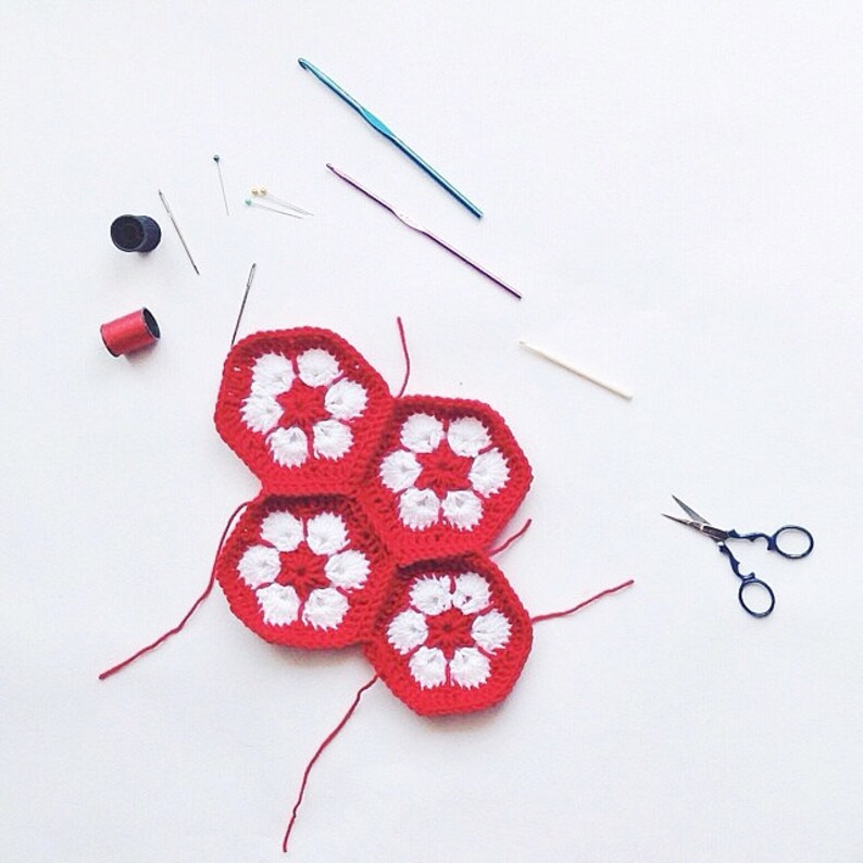 May include: A collection of crochet supplies on a white surface. The image features red and white crocheted hexagons, crochet hooks, needles, pins, scissors, and spools of thread. The hexagons are arranged in a cluster, showcasing the craft's vibrant colors.