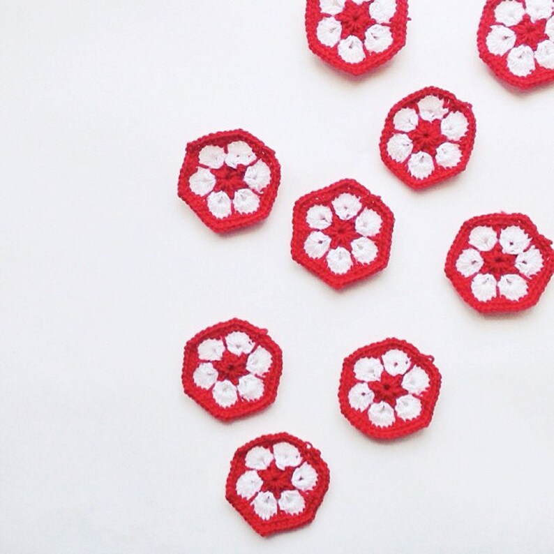 May include: A collection of seven small, hexagonal crochet motifs arranged in a scattered pattern. Each piece features a vibrant red center and border, with six white petal-like shapes forming a flower design in the middle of the hexagon.