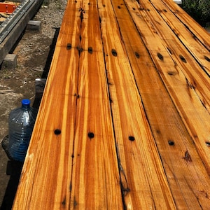 May include: Several long, rectangular wooden planks with a warm, orange-brown hue and prominent vertical grain patterns. The boards feature dark, circular knots and natural vertical fissures running along the length of the wood surface.
