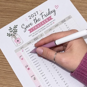May include: A 2027 Save the Friday tracker sheet featuring a table with columns for date, Friday, and amount to save. The document includes floral illustrations, a pink heart, and a piggy bank graphic. A pen is marking a checkbox on the list.
