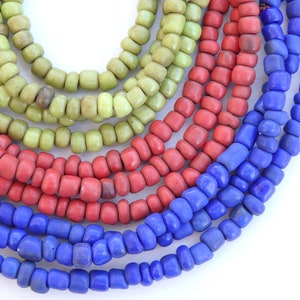 May include: A close-up of a multi-colored beaded necklace. The necklace is made of green, red, and blue beads. The beads are all different sizes and shapes.