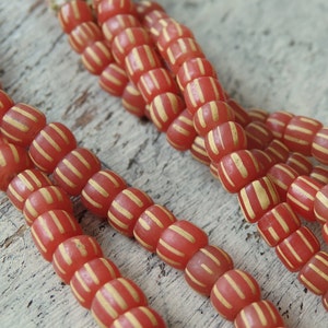 Può includere: Una collana di perline di vetro a strisce rosse e bianche. Le perline sono cilindriche e hanno una forma leggermente arrotondata. Le perline sono infilate su un filo trasparente.