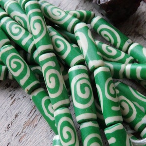 May include: A collection of green and white swirl-patterned beads. The cylindrical beads are a vibrant green with a cream-colored spiral design. The beads are strung together, suggesting they are for jewelry making or crafting.