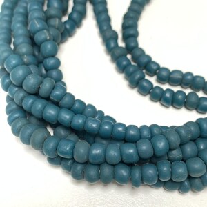 Peut inclure: Une collection de petites perles rondes et mates de couleur bleu sarcelle, enfilées sur plusieurs brins. Les perles présentent une texture uniforme et lisse ainsi qu'une teinte bleu-vert profonde et constante, disposées en un amas lâche.