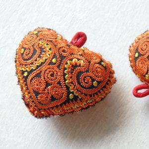 May include: Two embroidered heart-shaped ornaments with a black background and orange and yellow swirls.