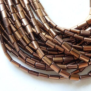 May include: A strand of brown metallic beads, each bead is a cylinder with a slightly rounded edge. The beads are arranged in a loose pile.
