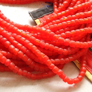 May include: A close-up of a long strand of bright red beads. The beads are round and have a slightly translucent appearance. The beads are arranged in a loose, flowing pattern.