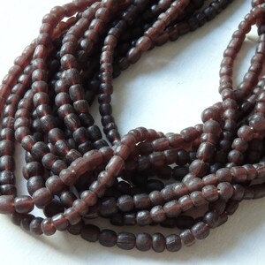 May include: A strand of dark brown glass beads. The beads are small and round, and they are strung together on a clear thread.