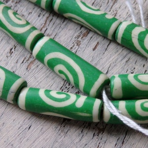 May include: Close-up of green and cream-colored wooden beads with a spiral design. The beads are cylindrical and strung together with white string. The beads are a vibrant green color with a cream-colored spiral pattern.