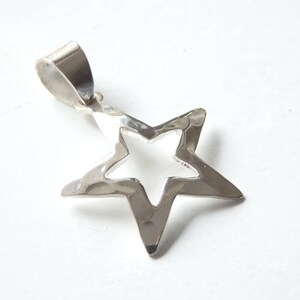 Peut inclure: Un pendentif en argent en forme d'étoile avec un motif découpé. Le pendentif a une boucle en haut pour l'attacher à une chaîne.