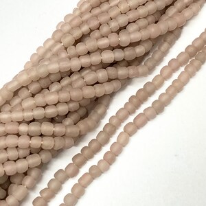 Könnte beinhalten: Eine Schnur aus hellrosa Glasperlen. Die Perlen sind klein und rund, mit einer matten Oberfläche. Sie sind auf einem durchsichtigen Faden aufgefädelt.