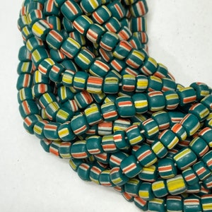 May include: A close-up of a strand of teal blue glass beads with white, yellow, and orange stripes. The beads are arranged in a random pattern, creating a visually appealing and colourful design.