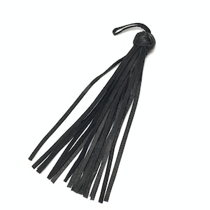 Könnte beinhalten: Ein schwarzer Lederquasten mit geknotetem Oberteil und mehreren langen, dünnen Streifen. Die Quaste wird wahrscheinlich zur Dekoration oder als Accessoire verwendet. Der Hintergrund ist schlicht weiß.