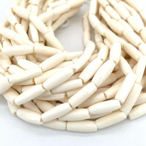 Peut inclure: Un brin de perles ovales lisses de couleur blanc cassé. Les perles sont en os et sont enfilées sur un cordon blanc.