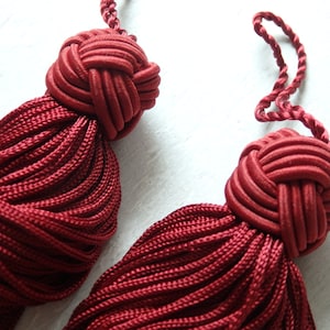 May include: Two burgundy tassel ornaments with a knotted top. The tassels are made of a soft, silky material.
