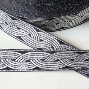 May include: Black and silver braided trim with a woven pattern. The trim is approximately 1 inch wide.