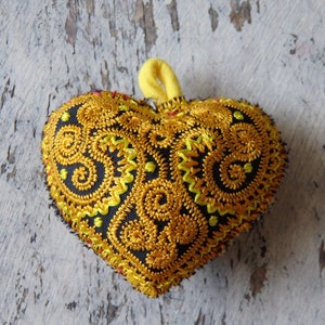May include: A heart-shaped decorative pillow with a black background and intricate yellow and gold embroidery.