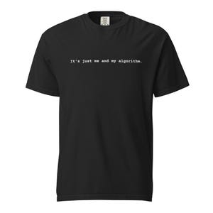 May include: A black short-sleeved t-shirt featuring the white typewriter-style text "It's just me and my algorithm." printed across the chest. The garment has a crew neckline and a standard fit, showcasing a clean and simple design aesthetic.