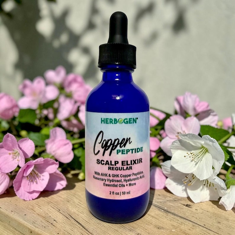 May include: A cobalt blue glass bottle with a black dropper cap containing Copper Peptide Scalp Elixir. The label features the text Herbogen, Copper Peptide Scalp Elixir Regular, and lists ingredients including AHK & GHK Copper Peptides, 2 fl oz | 59 ml.