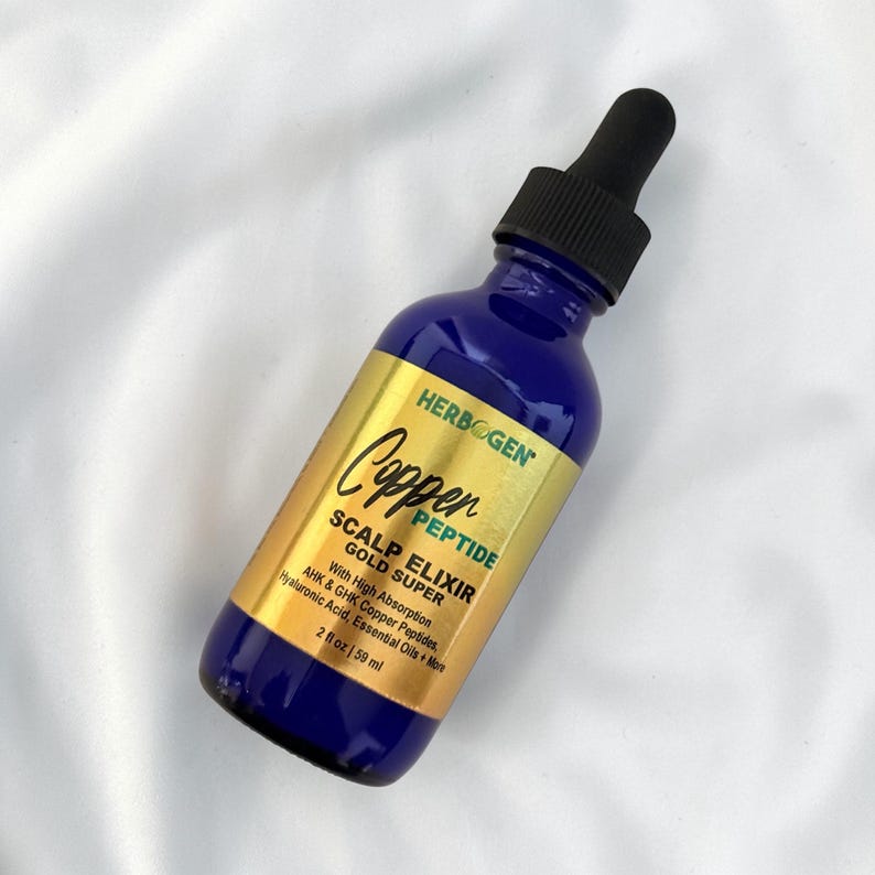 May include: A cobalt blue glass dropper bottle with a black cap and a gold label. The label reads HERBOGEN Copper PEPTIDE SCALP ELIXIR GOLD SUPER With High Absorption AHK & GHK Copper Peptides, Hyaluronic Acid, Essential Oils + More 2 fl oz | 59 ml.