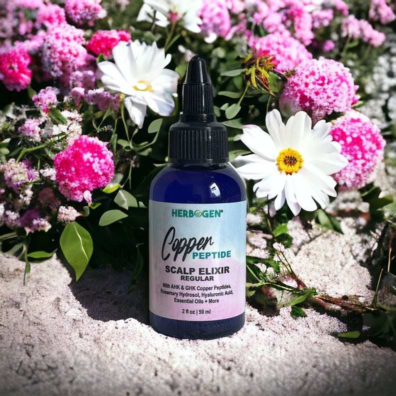 May include: A dark blue plastic bottle of Herbogen Copper Peptide Scalp Elixir with a black pointed cap. The label features the text Copper Peptide Scalp Elixir Regular with AHK & GHK Copper Peptides, Rosemary Hydrosol, Hyaluronic Acid, Essential Oils + More, and 2 fl oz | 59 ml.