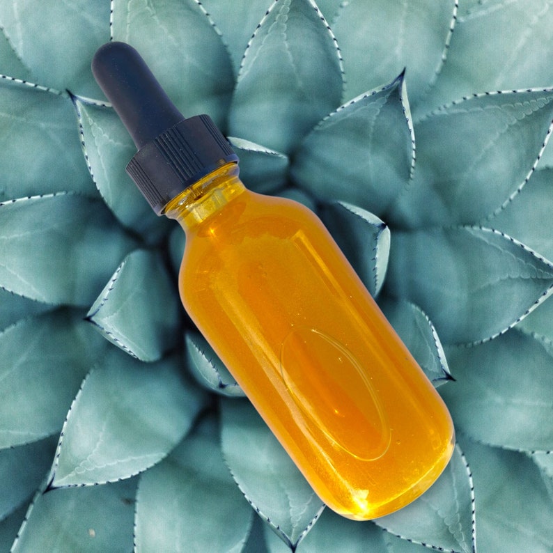 May include: A clear glass bottle with a black dropper top filled with a bright orange liquid. The bottle is sitting on a green leafy background.
