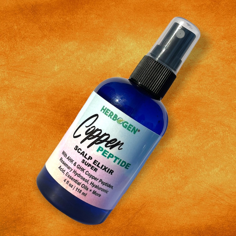May include: A blue plastic spray bottle containing Herbogen Copper Peptide Scalp Elixir Super. The white label features black text listing ingredients including AHK and GHK Copper Peptides, Rosemary Hydrosol, and Hyaluronic Acid, with 4 fl oz.