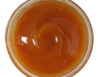 May include: A close-up view of a glass jar filled with a thick, orange-colored sauce. The sauce has a smooth, glossy texture and is swirling in the jar.