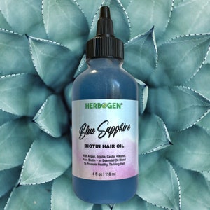 May include: A blue glass bottle with a black cap and label that reads "HERB GEN Blue Sapphire BIOTIN HAIR OIL With Argan, Jojoba, Castor + Monol Pure Biotin + an Essential Oil Blend To Promote Healthy, Thriving Hair 4 fl oz | 118 ml".