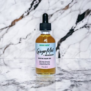 May include: A clear glass bottle with a black dropper top and a label that reads "HERBOGEN Ginger Mint + ROSEMARY BIOTIN HAIR OIL With Ginger, Rosemary, Peppermint Oil + Biotin To Support Healthy Hair 2 fl oz | 59 ml"