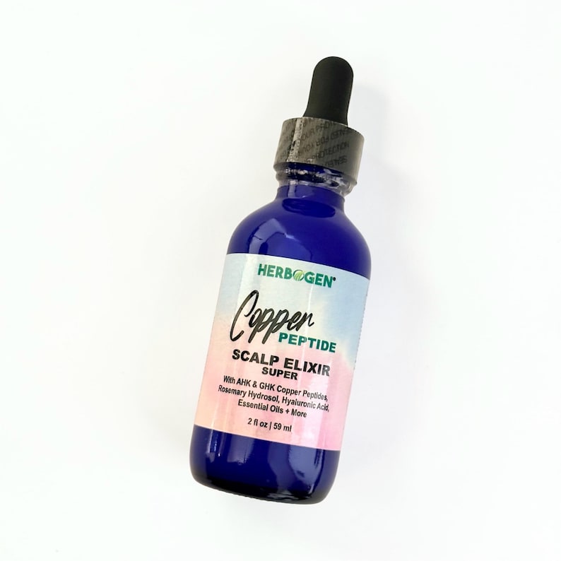 May include: A cobalt blue glass bottle with a black dropper cap containing Herbogen Copper Peptide Scalp Elixir Super. The label features a gradient background and lists ingredients including AHK and GHK copper peptides, rosemary hydrosol, hyaluronic acid, and essential oils. The bottle contains 2 fl oz.