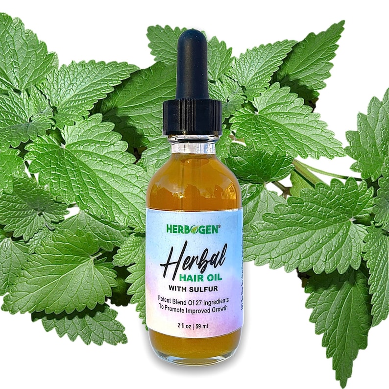 May include: A clear glass bottle with a black dropper top, labeled "HERBOGEN Herbal HAIR OIL WITH SULFUR". The bottle contains a yellow liquid and is surrounded by green leaves. The label also states "Potent Blend Of 27 Ingredients To Promote Improved Growth" and "2 fl oz | 59 ml".
