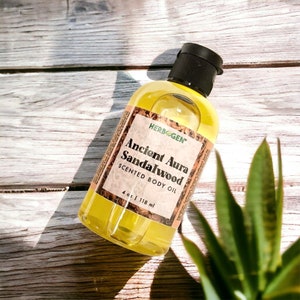 May include: A clear glass bottle of Ancient Aura Sandalwood Scented Body Oil by Herbogen. The bottle is 4 oz or 118 ml and is sitting on a wooden surface.