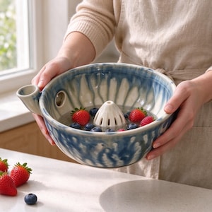 May include: A ceramic berry colander bowl featuring a blue and white marbled glaze finish. The bowl includes a central raised cone for rinsing fruit, a side pouring spout, and a small drainage hole. Fresh strawberries and blueberries are inside.