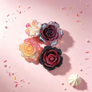 May include: Four decorative flower-shaped resin pieces featuring glittery finishes. One is white with pink accents, one is a translucent dark purple, one is a peach-orange blend, and one is a deep red with a black glittery outer petal layer.