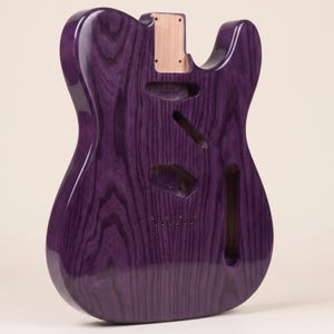 Puede incluir: Un cuerpo de guitarra eléctrica de cuerpo sólido con un acabado en color púrpura intenso y un patrón de veta de madera visible. El cuerpo presenta un bolsillo para el mástil, cavidad para el puente, cavidad de control y ranuras para pastillas.