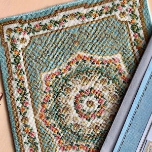 Puede incluir: Un patrón de punto de cruz terminado de una alfombra azul y blanca con un diseño floral. El patrón se llama "de Malmanche Demesne" y mide 137 mm x 186 mm (5 3/8" x 7 1/4") trabajado en lienzo de 22ct. El patrón es de ellijenks.com.