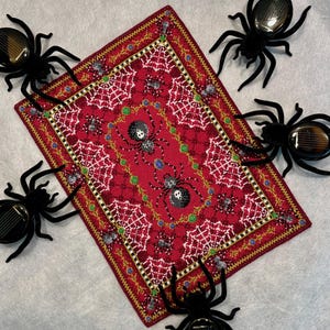 May include: A red and gold embroidered rug with a spiderweb design and black spiders. The rug is surrounded by black spiders with red eyes.
