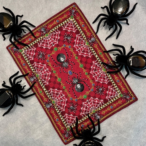 Könnte beinhalten: Ein roter und goldfarbener bestickter Teppich mit einem Spinnennetz-Design und schwarzen Spinnen. Der Teppich ist von schwarzen Spinnen mit roten Augen umgeben.