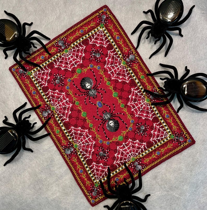 May include: A red and gold embroidered rug with a spiderweb design and black spiders. The rug is surrounded by black spiders with red eyes.