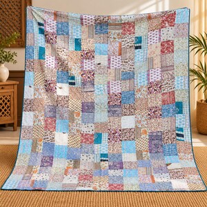 May include: A rectangular quilt featuring a patchwork design composed of numerous small, multi-coloured fabric squares. The quilt displays a variety of floral, geometric, and abstract patterns in shades of blue, red, purple, white, and tan.