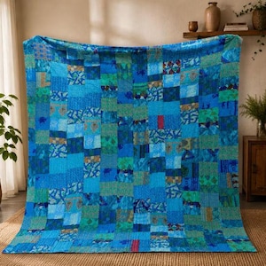 May include: A rectangular quilt featuring a patchwork design composed of various shades of blue, teal, and green fabric squares. The textile displays intricate, fine stitching patterns throughout, creating a textured surface with diverse geometric and floral motifs.