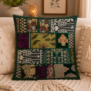 May include: A square throw pillow featuring a patchwork design of dark green fabric panels. The panels are decorated with intricate embroidery, gold metallic thread, beadwork, and floral patterns. A dark green border frames the entire pillow.